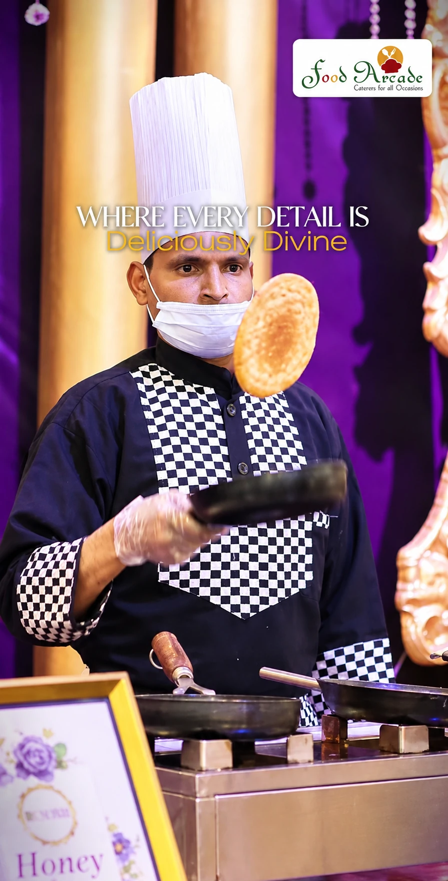 Chef in a checked jacket tossing a flatbread above a frying pan at a purple and gold counter