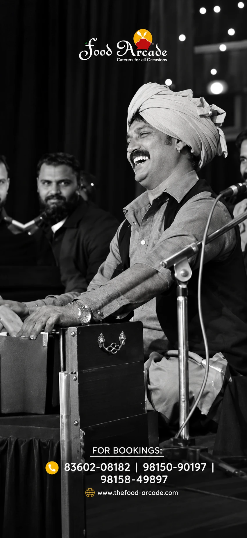 Black and white photo of a musician laughing as he plays a harmonium on stage