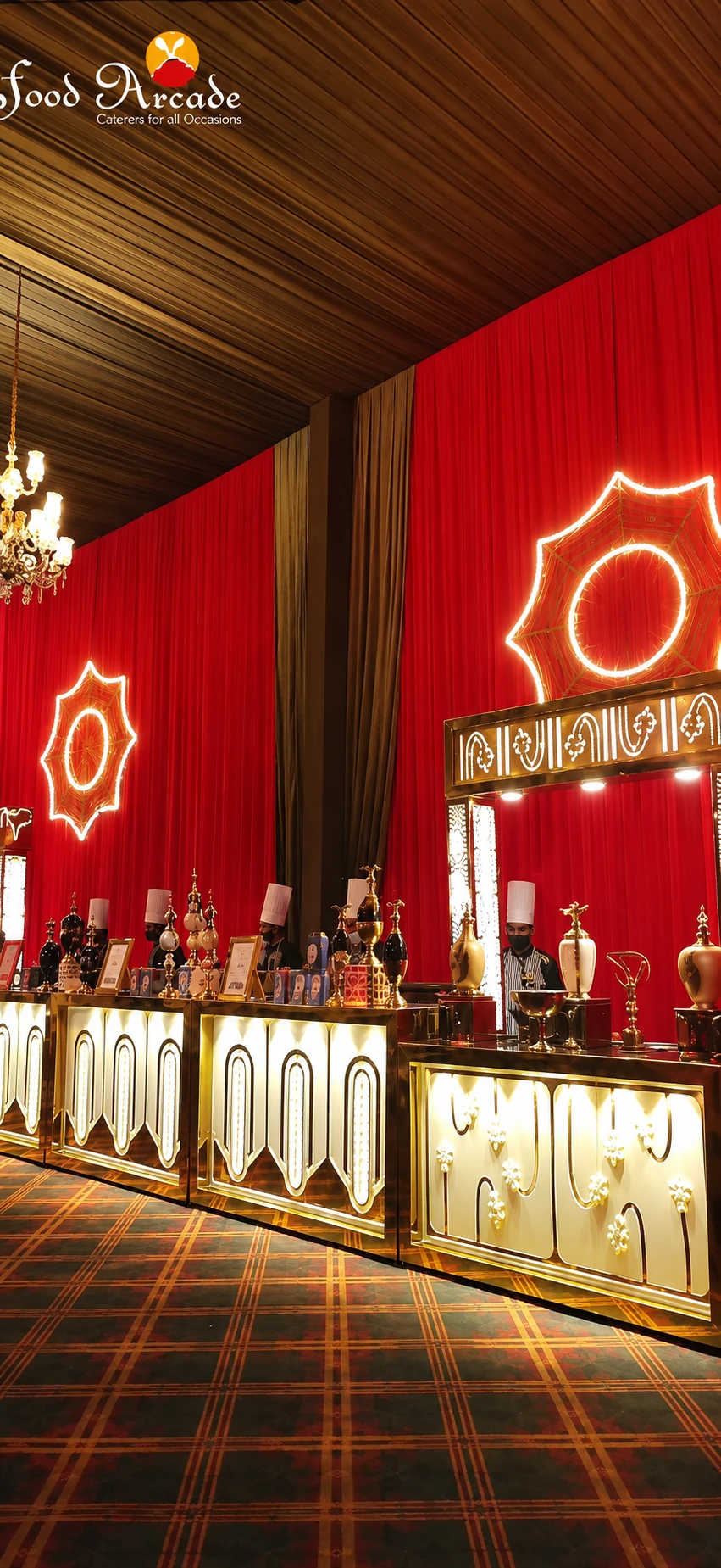 Row of gold and white lit counters with chefs behind them against red drapes and glowing ornaments